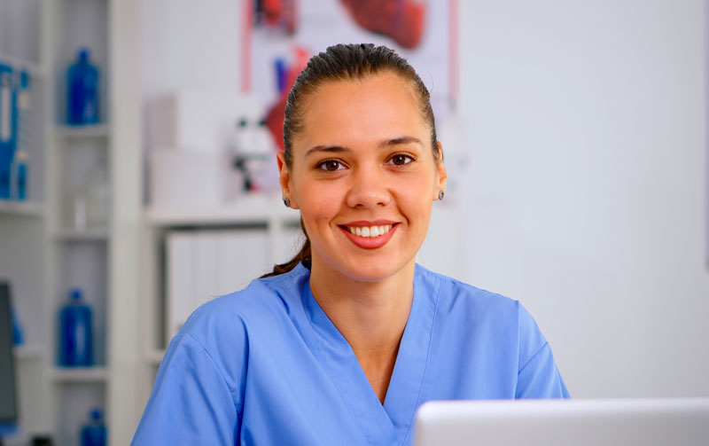 close up young medical assistant typing laptop raising head smiling camera sitting hospital office wearing blue uniform hospital healthcare worker medicine clinical assistant health